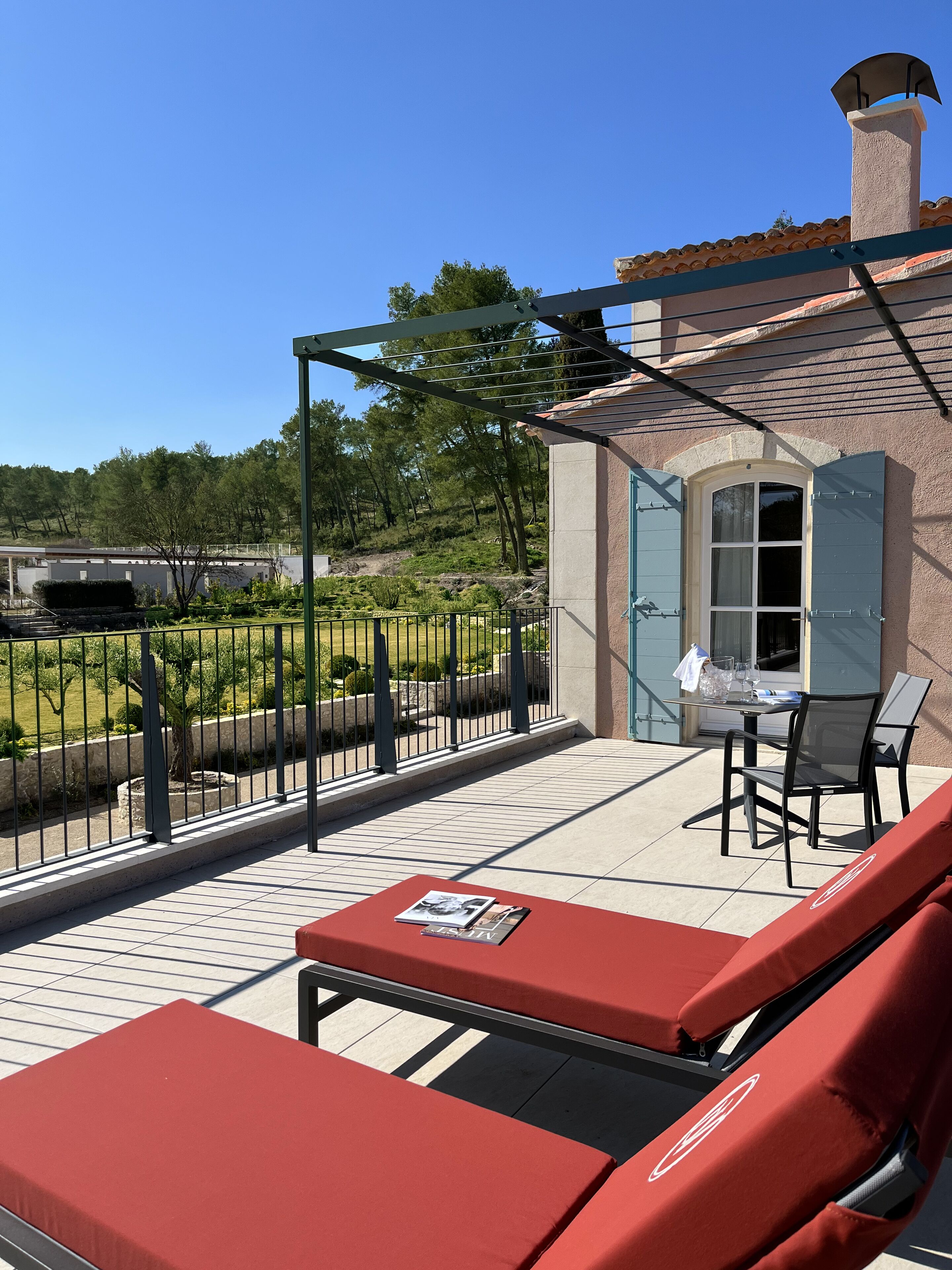 A balcony with red cushioned seating, a table with a glass, and a view of a garden and trees.