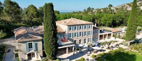 A large, multi-story building with a Mediterranean architectural style, featuring a mix of stone and stucco exteriors, multiple balconies, and a well-maintained garden with pathways and greenery.