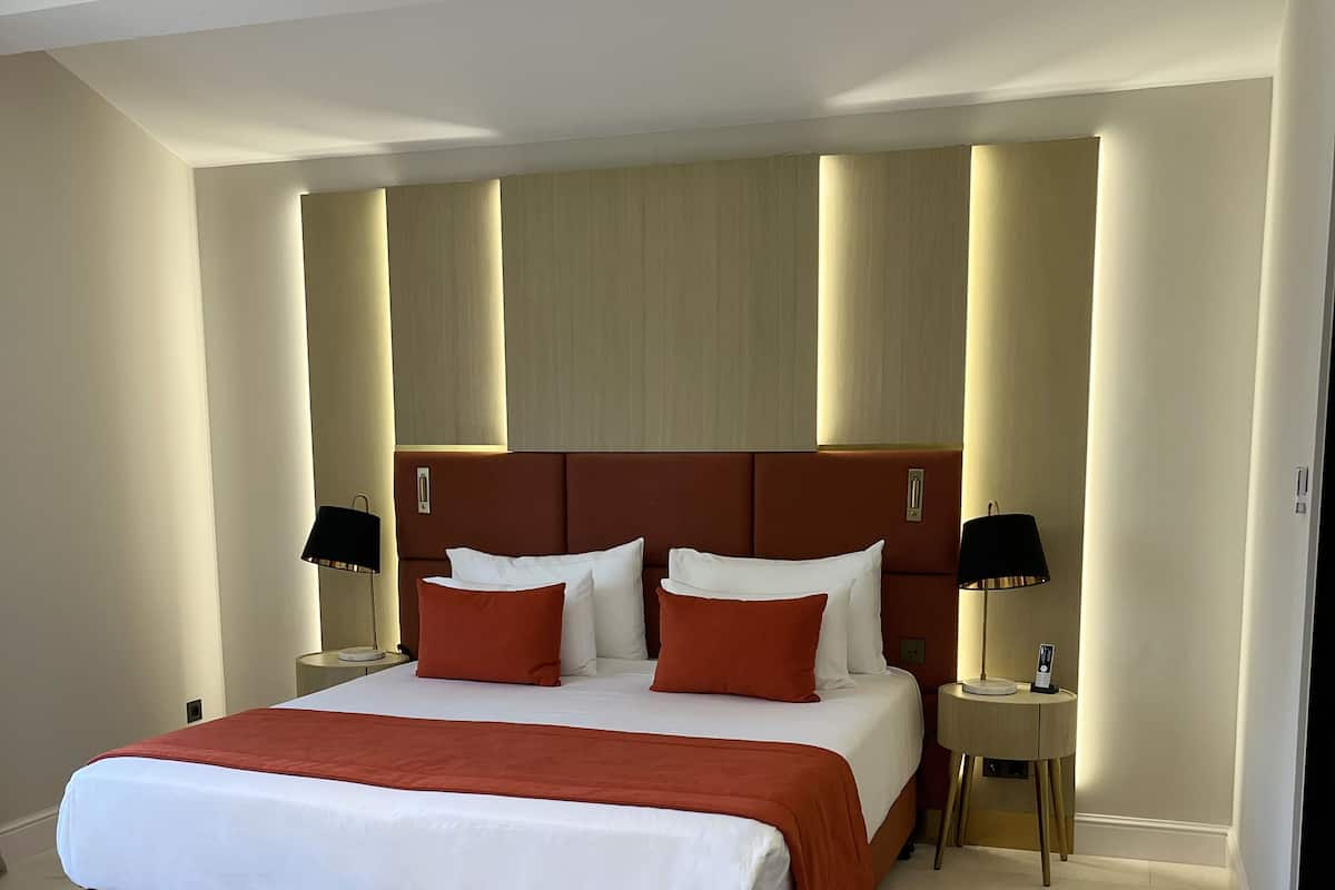 A modern hotel room with a large bed, a bedside table with a lamp, and a small table with a phone.