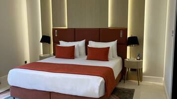 Una habitación de hotel moderna con una cama grande, una mesita de noche con una lámpara y una pequeña mesa con un teléfono.