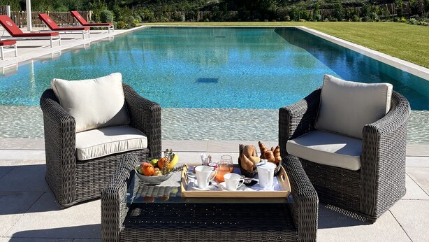 A poolside area with wicker chairs, a tray table with breakfast items, and a clear blue pool. - Domaine de Valmouriane (St.-Rémy-de-Provence)
