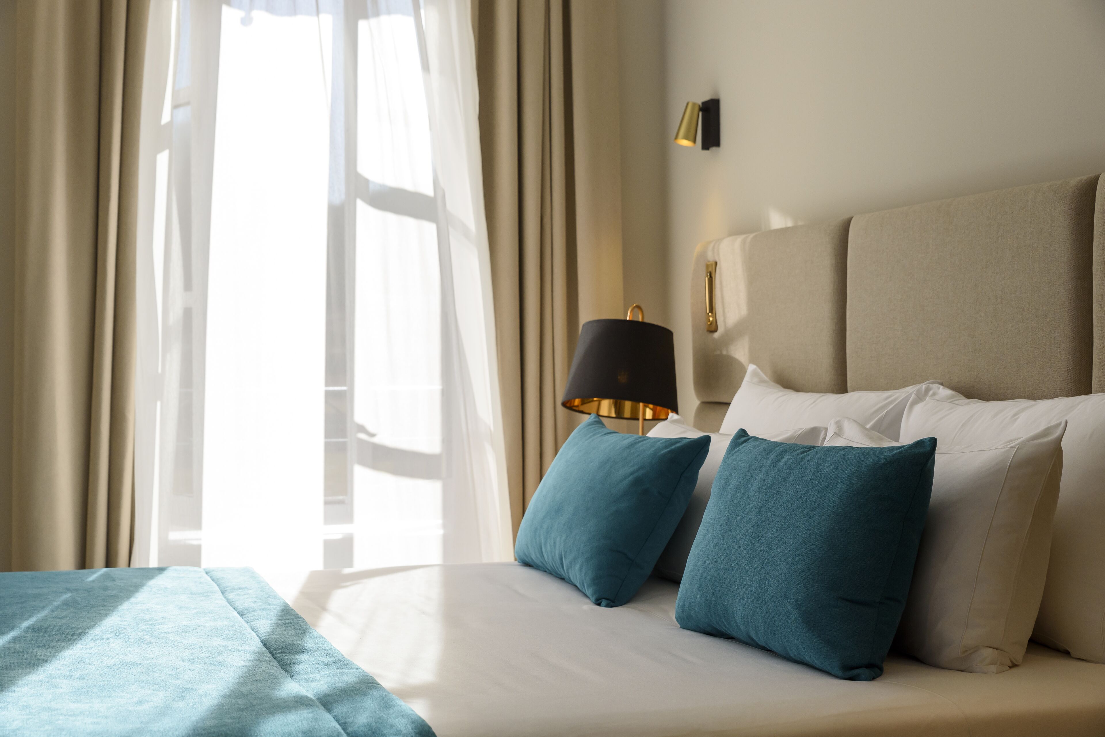 A hotel room with a bed, two pillows, a lamp, and a window with curtains.