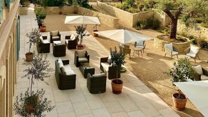 A sunlit outdoor patio with wicker furniture, potted plants, and umbrellas. - Domaine de Valmouriane (St.-Rémy-de-Provence)