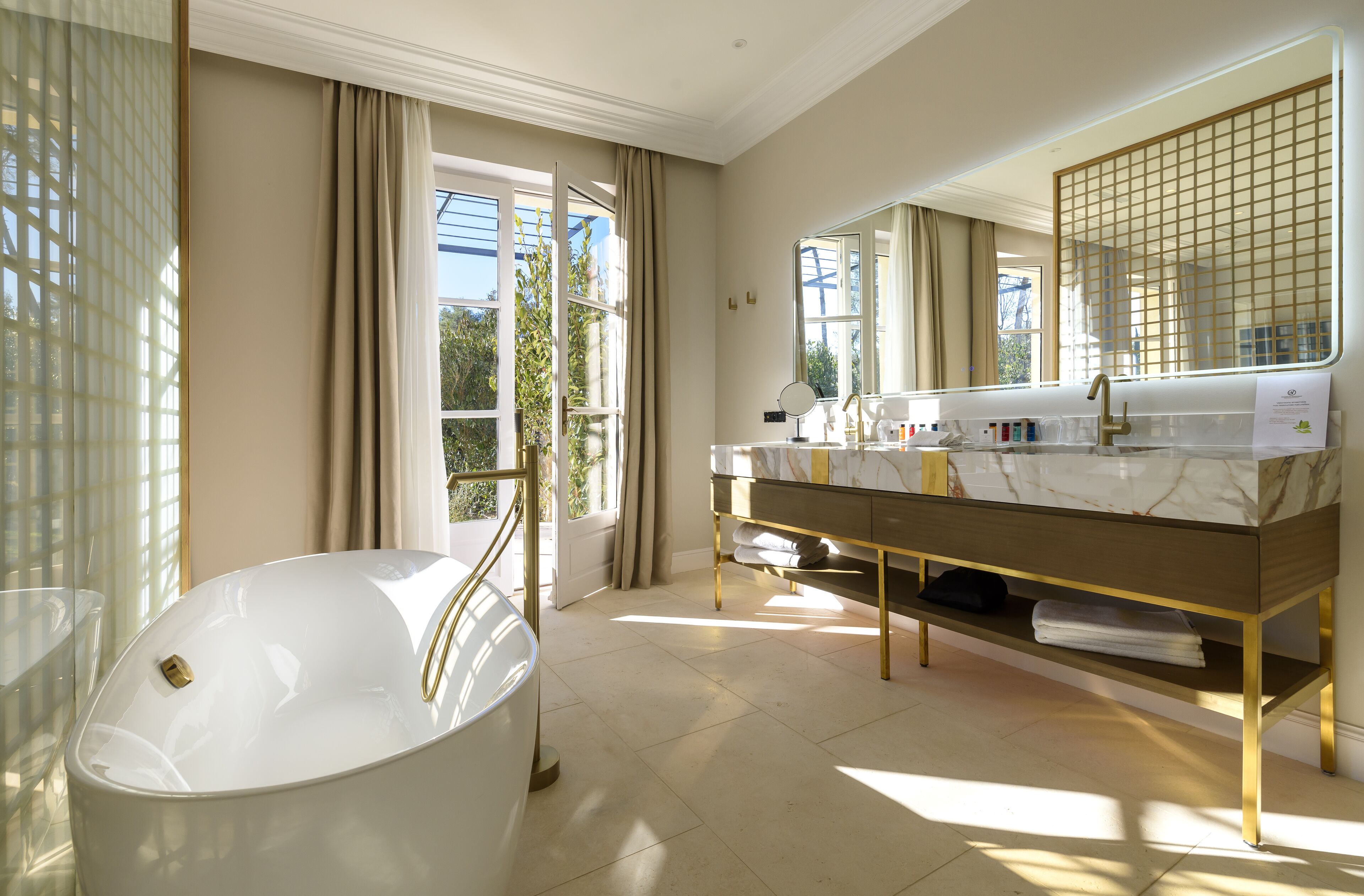 Ein modernes Badezimmer mit freistehender Badewanne, einem Waschtisch mit großem Spiegel und einem Fenster mit Vorhängen.