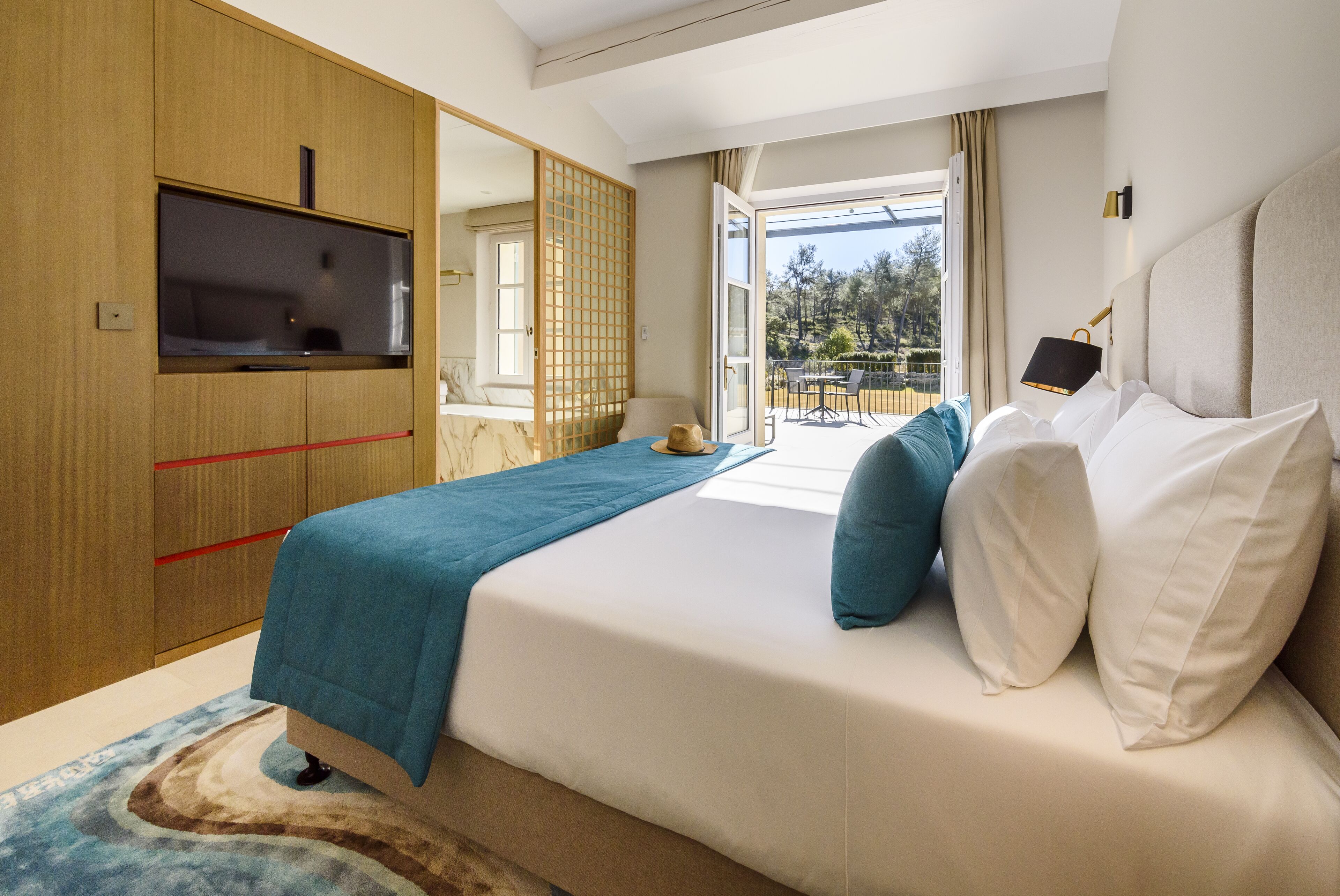 Un dormitorio con cama, televisión, puerta corredera y vistas al exterior.