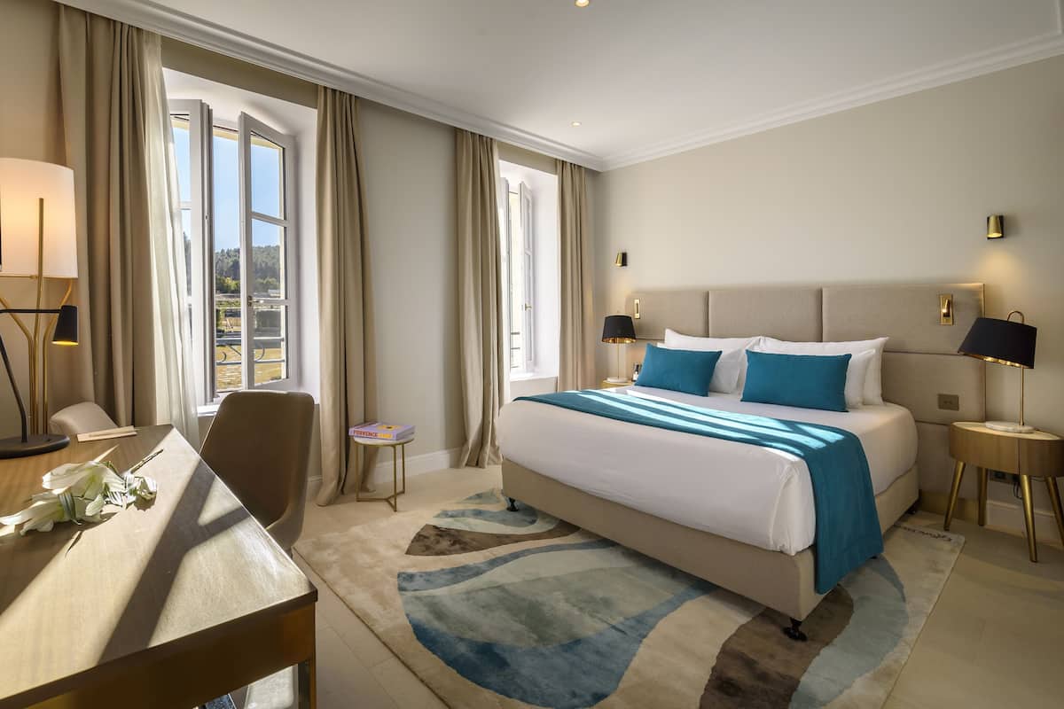A hotel room with a bed, bedside tables, a desk, and a chair.