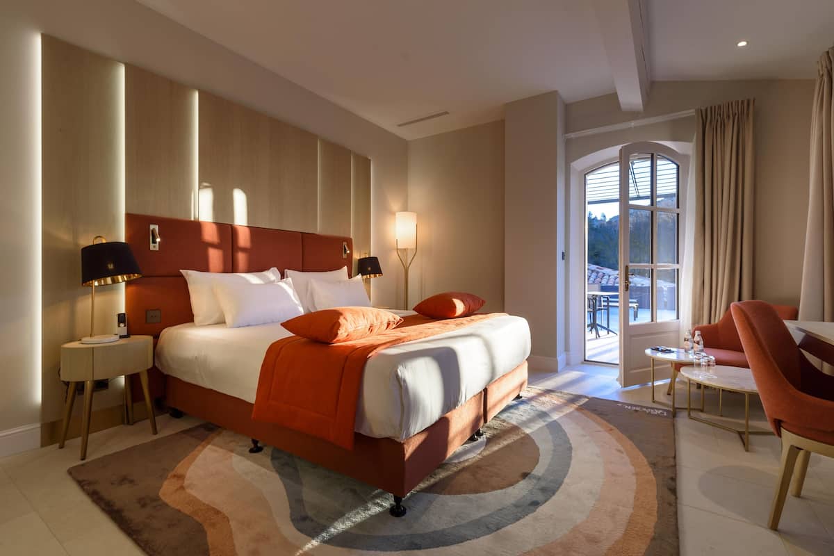 A hotel room with a large bed, a sitting area with a table and chairs, and a view through a glass door.