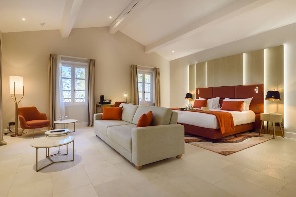 A modern hotel room with a large bed, a sofa, a coffee table, and a chair.