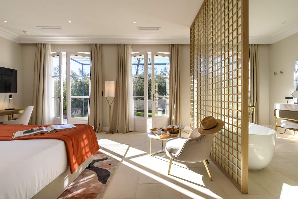A hotel room with a large bed, a desk, a chair, a small table, and a bathroom.
