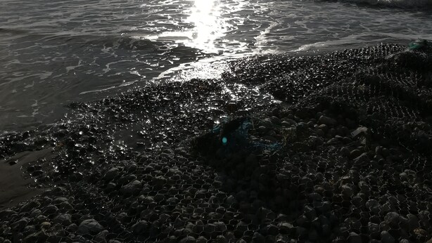 Een strand met een reflectie van de zon op het water, een heldere lucht en een rotsachtige kustlijn.