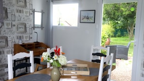 Een eetruimte met een houten tafel, witte stoelen, een vaas met bloemen en een raam met uitzicht op groen.