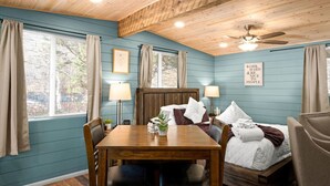 A cozy room with a wooden ceiling, a bed with white bedding, a dining table with chairs, and a wall-mounted lamp. - 18 Creekside Retreat (Sedona)