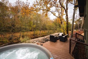 A hot tub on a wooden deck with outdoor furniture, surrounded by autumn foliage.