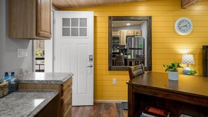 Une cuisine avec des meubles de rangement en bois, une porte blanche, une horloge au mur et une table à manger avec des chaises.