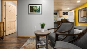 Une pièce avec une porte en bois, un tableau encadré représentant une forêt, une petite table ronde avec une plante et un canapé gris.