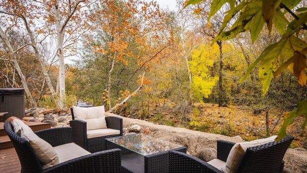 An outdoor patio with wicker furniture and a glass table, surrounded by autumn foliage. - 15 Creekside Retreat (Sedona)