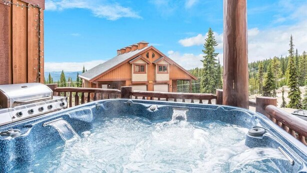 Un bain à remous avec une terrasse en bois et une vue sur un chalet situé dans une zone boisée.