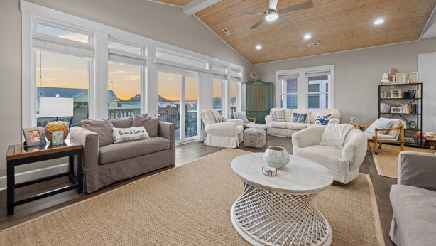 A spacious living room with a high ceiling, large windows, and a view of the sunset. - Gemini Dream #102 - Soundfront w/ Pool, Boat Dock, Elevator, Dogs Allowed! (Topsail Beach)