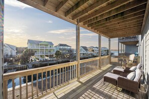Eine Holzterrasse mit Korbmöbeln mit Blick auf einen Yachthafen mit Booten und Häusern.