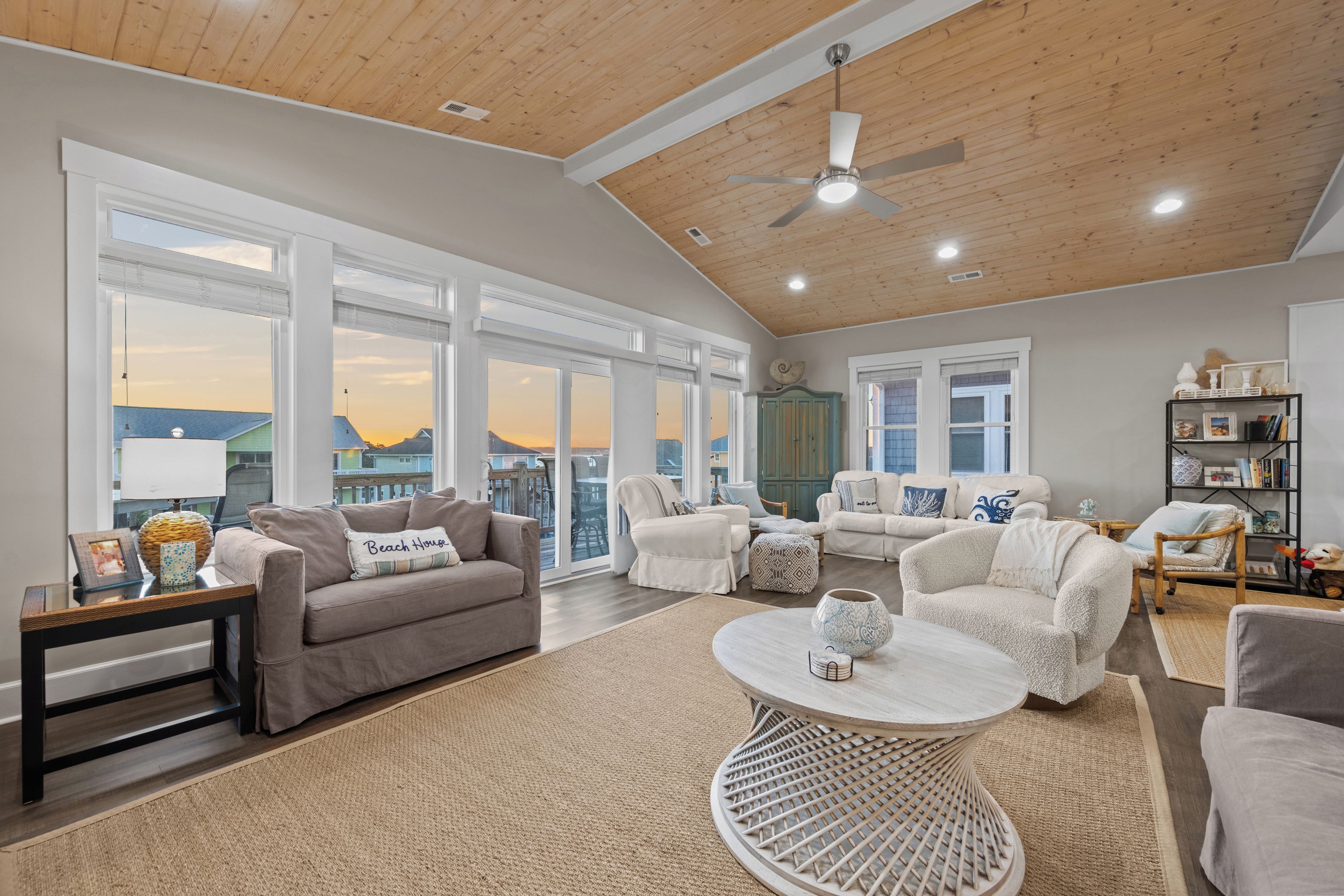 A spacious living room with a high ceiling, large windows, and a view of the sunset.