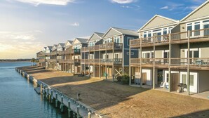 A waterfront property with multiple-story buildings, a wooden dock, and a grassy area. - Gemini Dream #102 - Soundfront w/ Pool, Boat Dock, Elevator, Dogs Allowed! (Topsail Beach)
