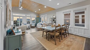 A spacious living area with a high ceiling, wooden beams, and a dining table with chairs. - Gemini Dream #102 - Soundfront w/ Pool, Boat Dock, Elevator, Dogs Allowed! (Topsail Beach)