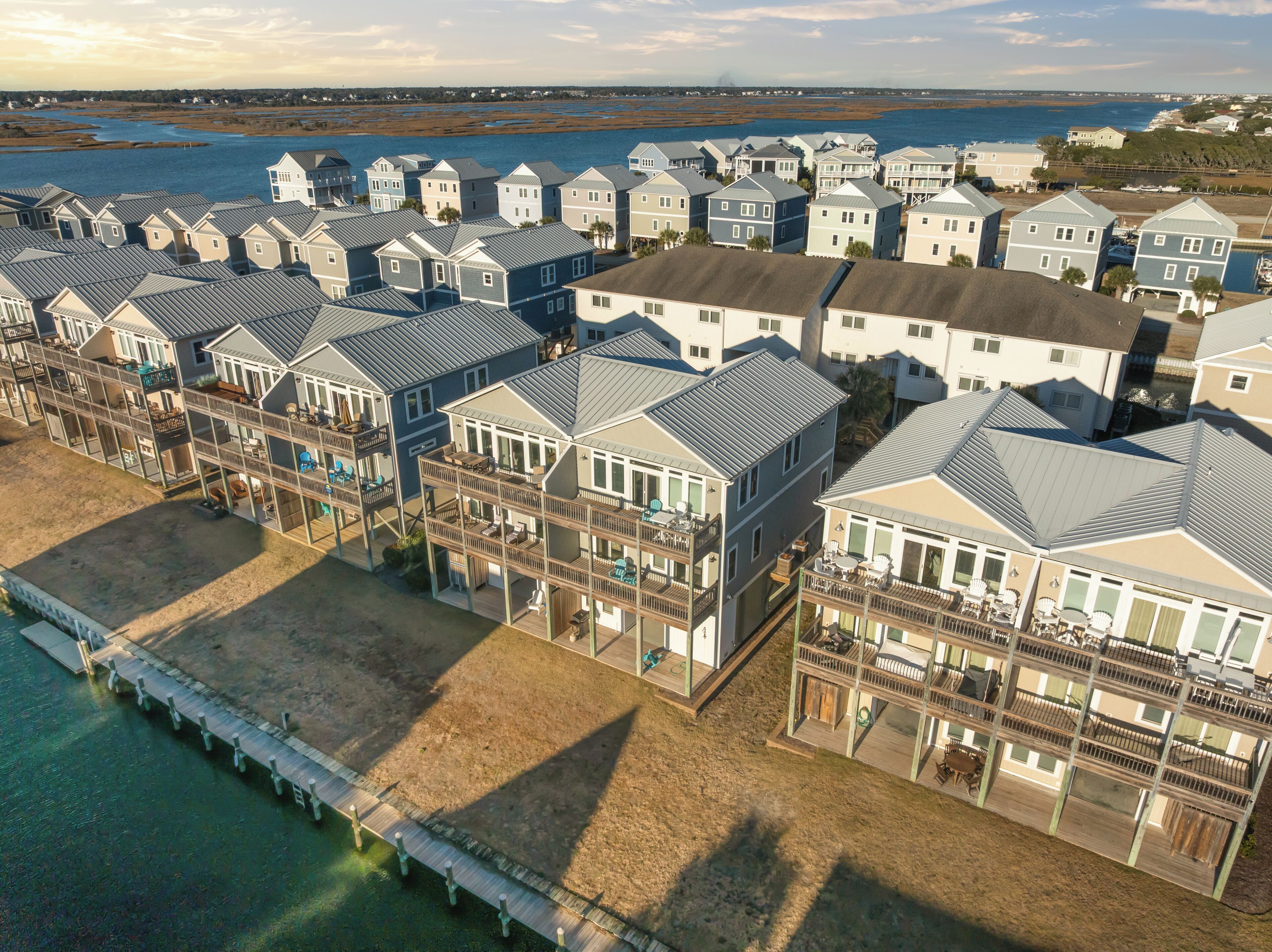A coastal residential area with multiple two-story houses featuring balconies, a pier, and a view of the ocean.