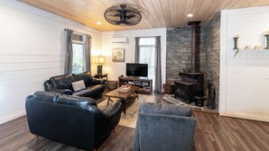 Ein gemütliches Wohnzimmer mit einer schwarzen Ledersofa, einem grauen Sessel, einem Holztisch und einem Kamin aus Stein.