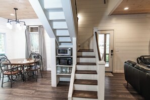 Een moderne keuken met een inbouwmagnetron en oven, een eetgedeelte met een houten tafel en metalen stoelen, en een trap met houten balustrade.