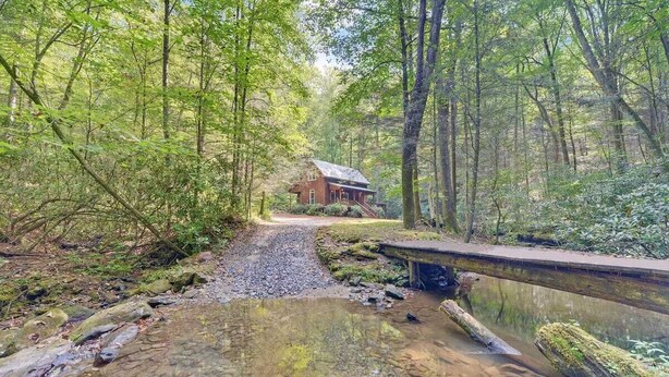 Eine rustikale Holzhütte im Wald, umgeben von dichten Bäumen und einem kleinen Bach.