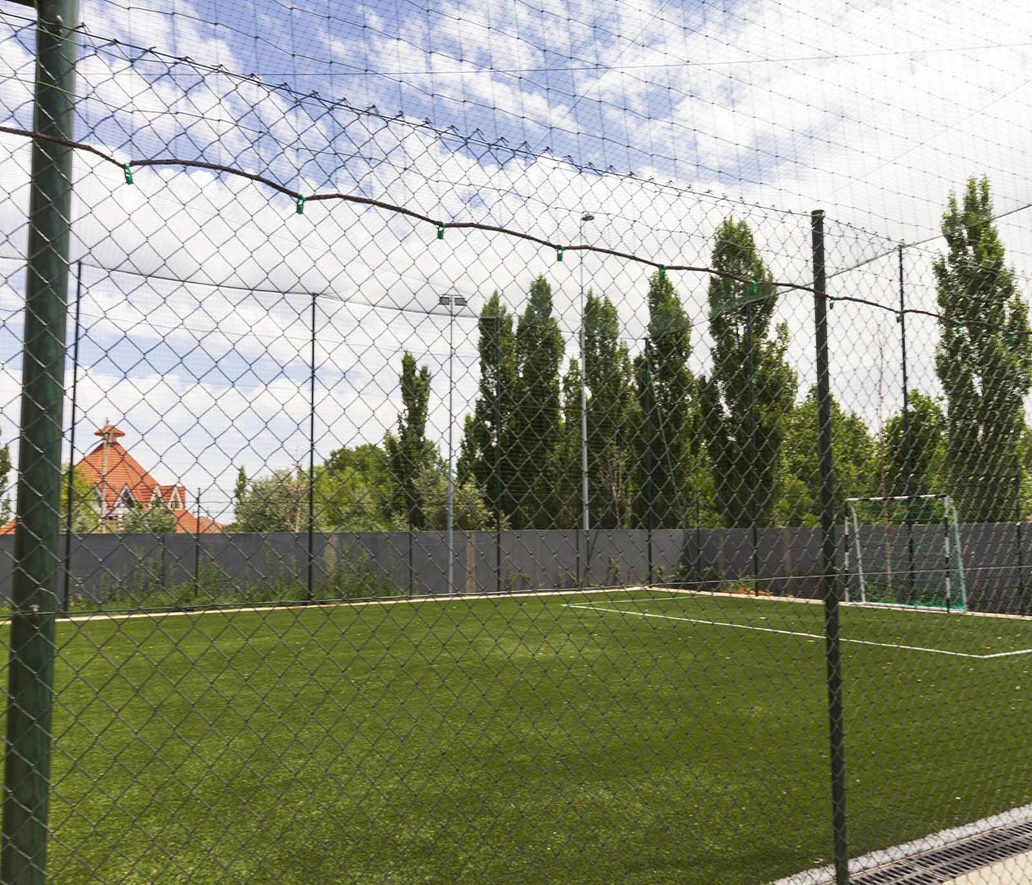 A fenced sports field with a clear sky and trees in the background.