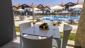 A table with a fruit bowl and two glasses of wine, overlooking a pool area with umbrellas and lounge chairs. - Zephyr Ifrane (Ifrane)