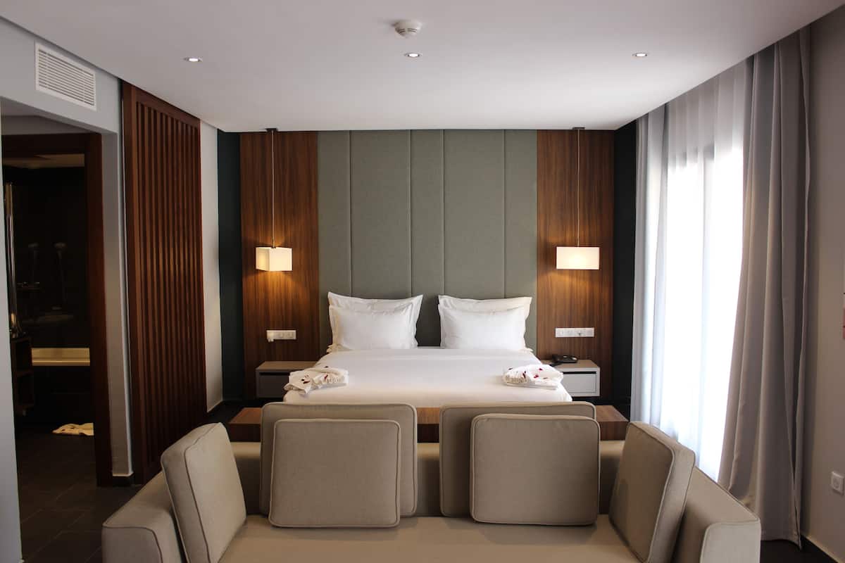 Habitación de hotel con una cama grande, dos lámparas de noche, un cabecero de madera y un espacio de descanso con dos sillones.