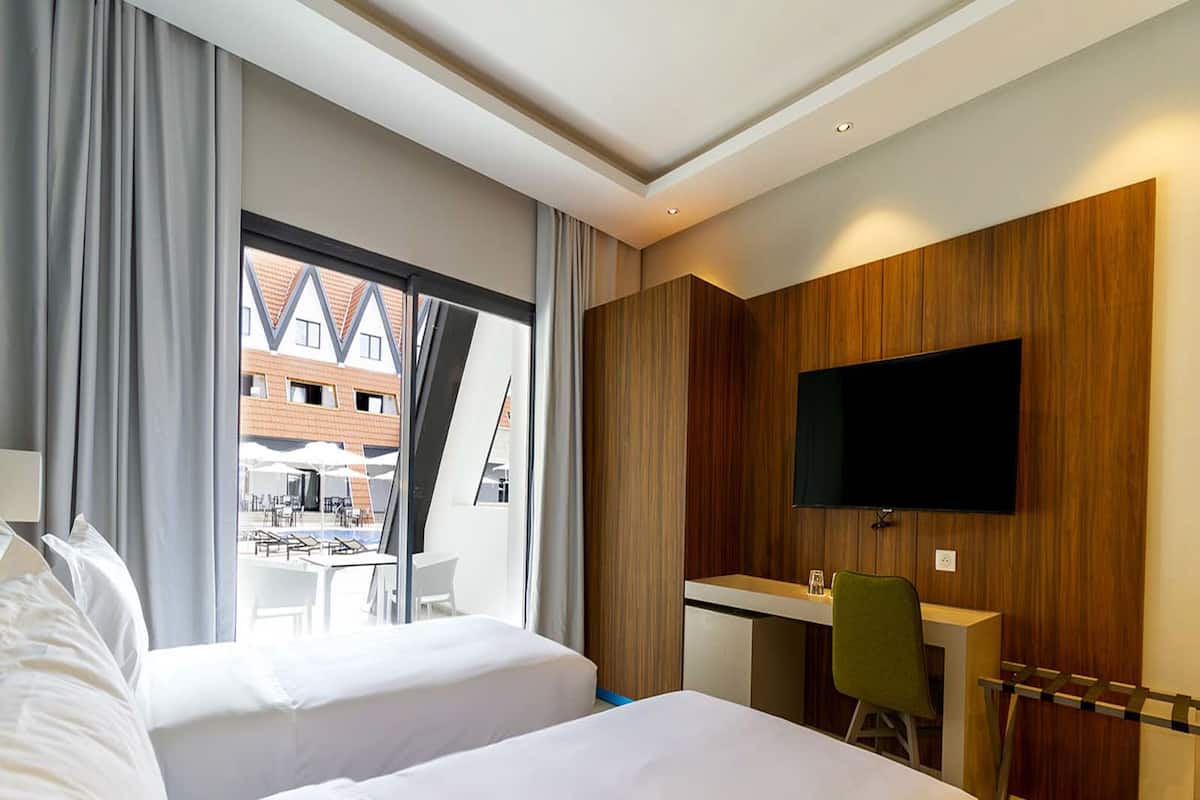 Habitación de hotel con dos camas, un escritorio, una silla, un televisor y vistas al exterior.
