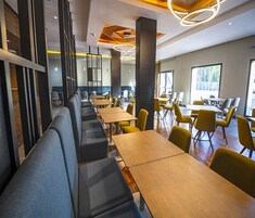 Un espace de restauration moderne, doté de longues tables et de banquettes, de grandes fenêtres et d’un design contemporain au niveau du plafond.
