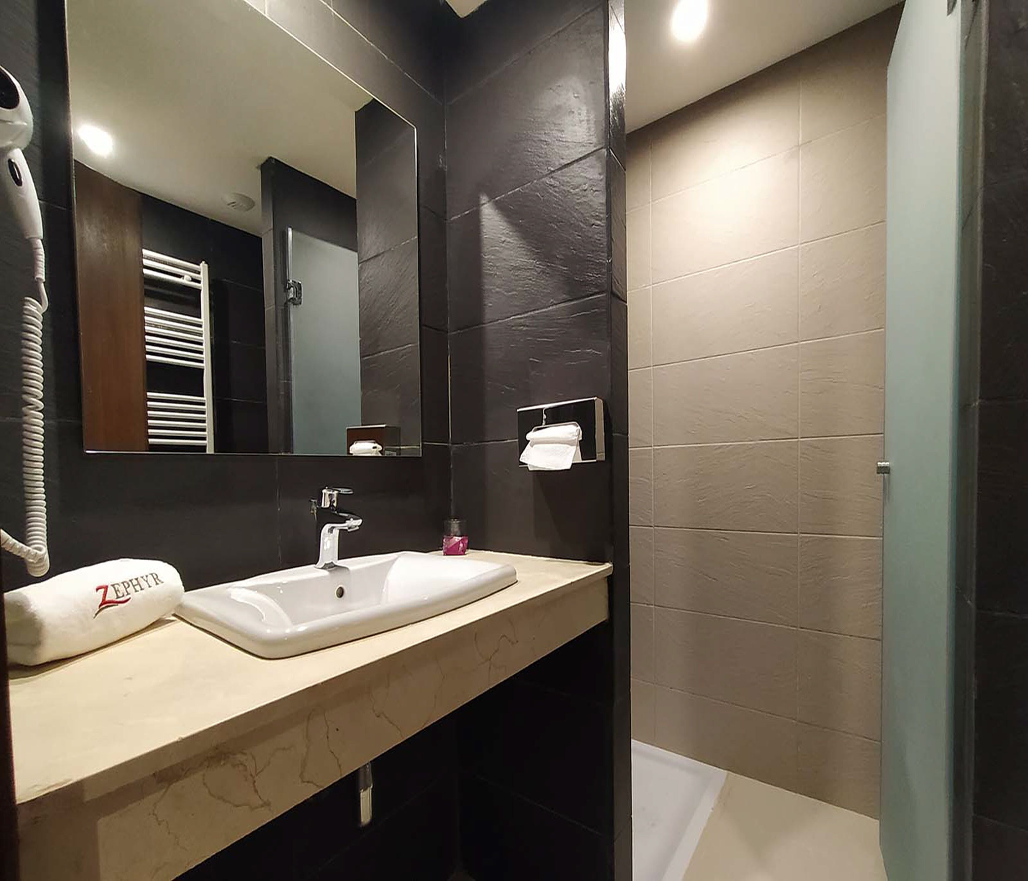 A modern bathroom with two sinks, a large mirror, and dark tiled walls.