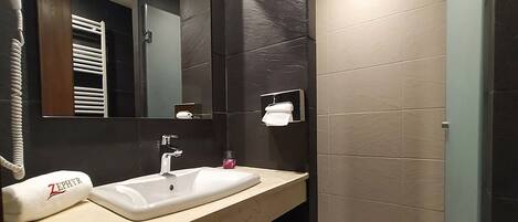 A modern bathroom with two sinks, a large mirror, and dark tiled walls.