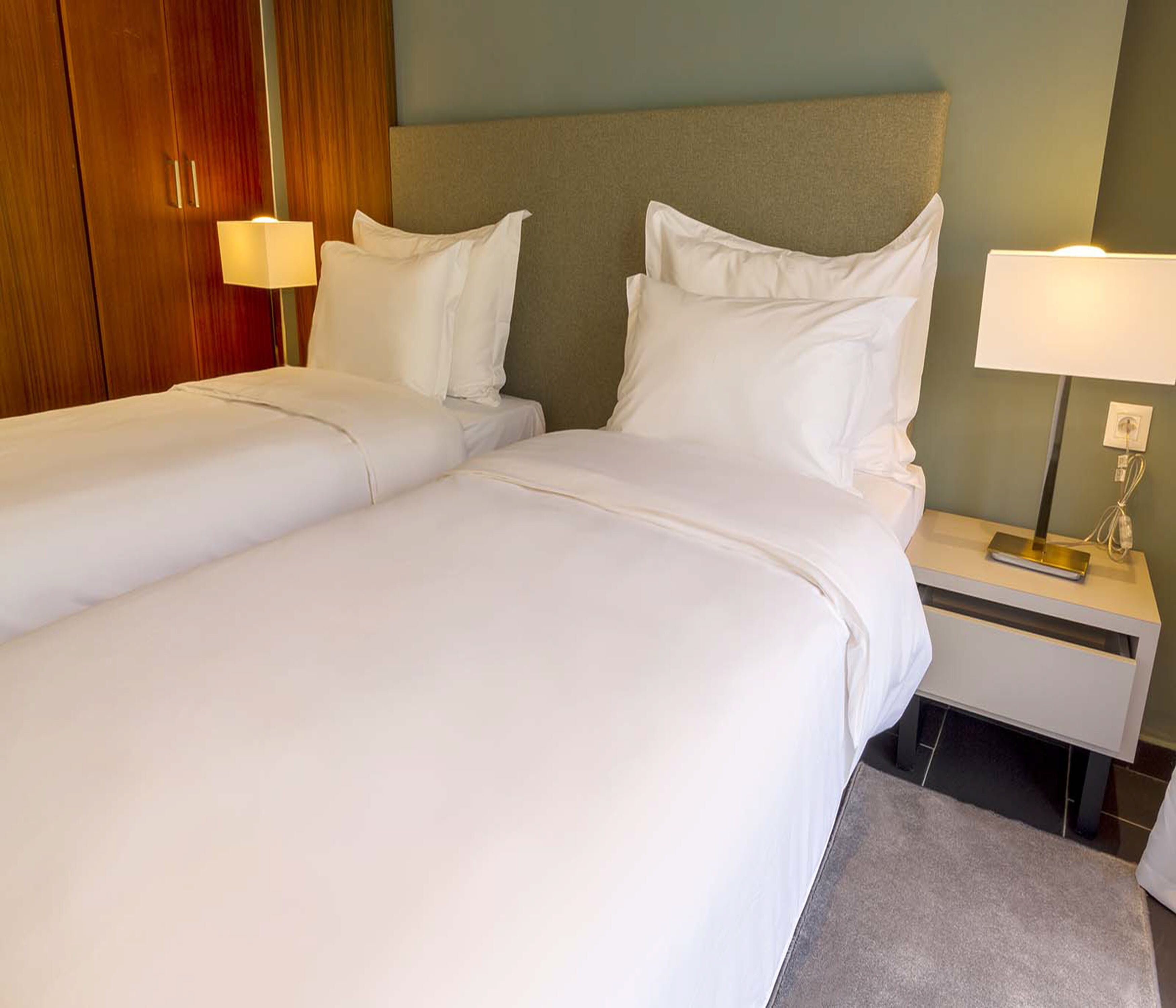 A hotel room with two single beds, a nightstand with a lamp, and a wooden wardrobe.