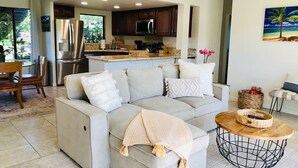 A modern living room with a grey sofa, a coffee table, and a kitchen in the background. - Mamalahoa Mountain View Luxury Condo (Princeville)