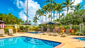 A swimming pool with lounge chairs and umbrellas, surrounded by palm trees and tropical plants. - Mamalahoa Mountain View Luxury Condo (Princeville)