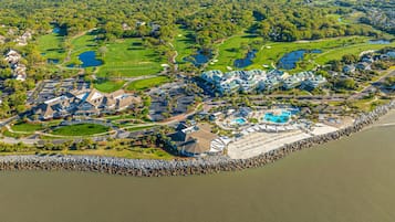An aerial view of a coastal resort with a golf course, a large pool, and beachfront villas.