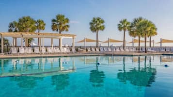 A clear blue pool with lounge chairs and palm trees.
