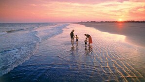 A beach scene with a sunset, calm water, and people standing in shallow water. - 1315 Pelican Watch Villas Beach & Free Amenities - Sale 249 USD (Seabrook Island)