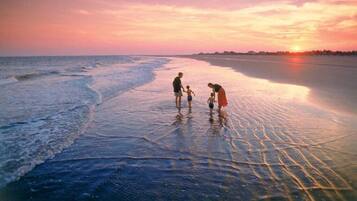 A beach scene with a sunset, calm water, and people standing in shallow water.