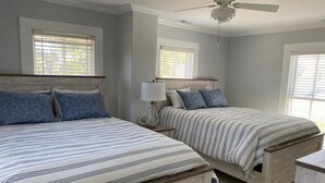 Un dormitorio con dos camas, un ventilador de techo y ventanas con persianas.