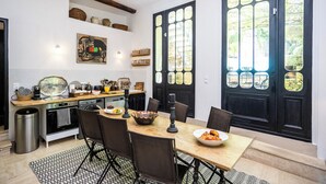 A dining area with a table set for two, a chandelier, and a kitchen in the background. - Villa Ocre Menerbes Panoramic view Swimming pool Garden Terraces (MENERBES)