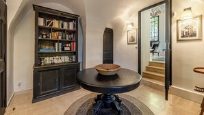 A hallway with a bookshelf, a round table with a woven basket, and a staircase leading to another room. - Villa Ocre Menerbes Panoramic view Swimming pool Garden Terraces (MENERBES)