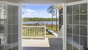Blick aus einem Zimmer mit Glastür auf eine Terrasse mit Blick auf einen See, eine Holzterrasse und ein Schild mit der Aufschrift 'WELCOME'.