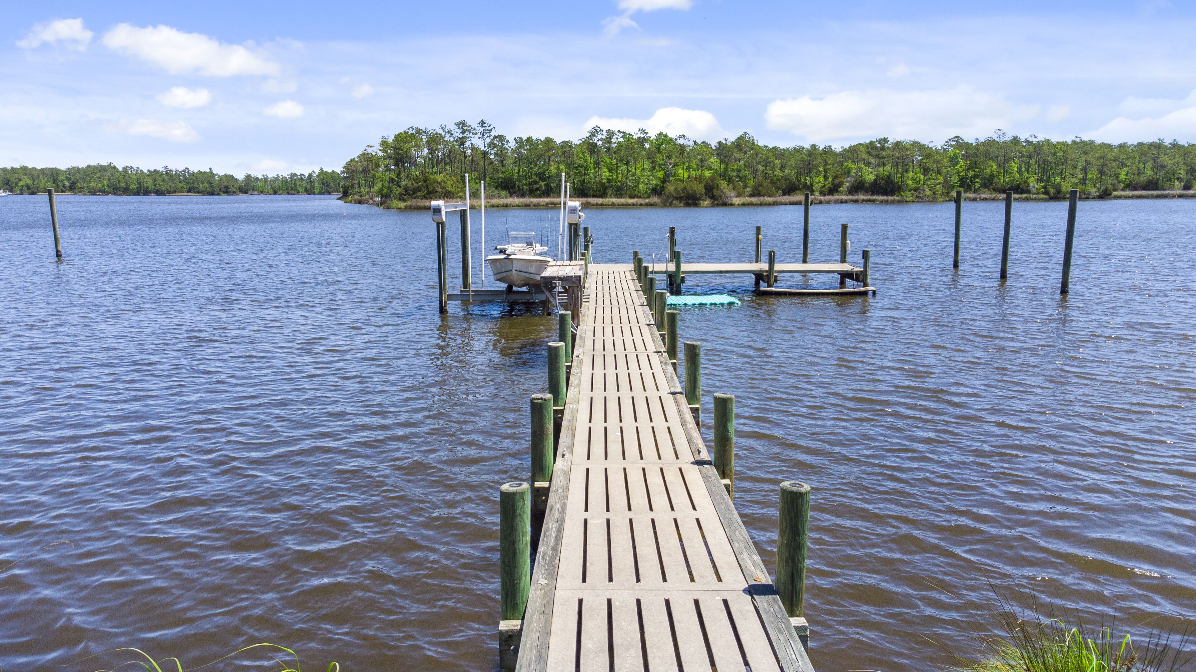 Un muelle de madera que se adentra en un lago tranquilo, rodeado de árboles.