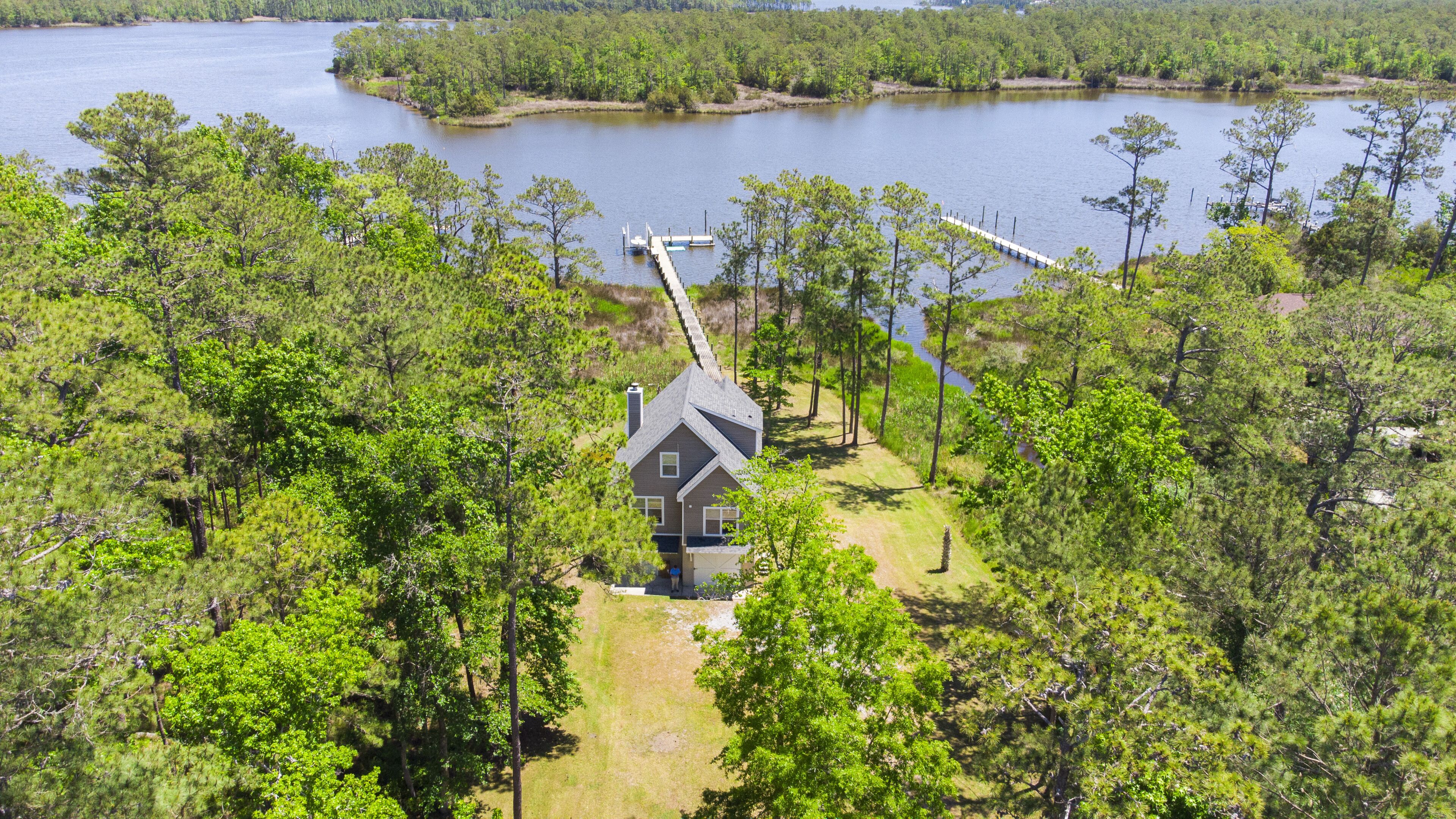 A house surrounded by dense forest, with a dock extending into a lake.